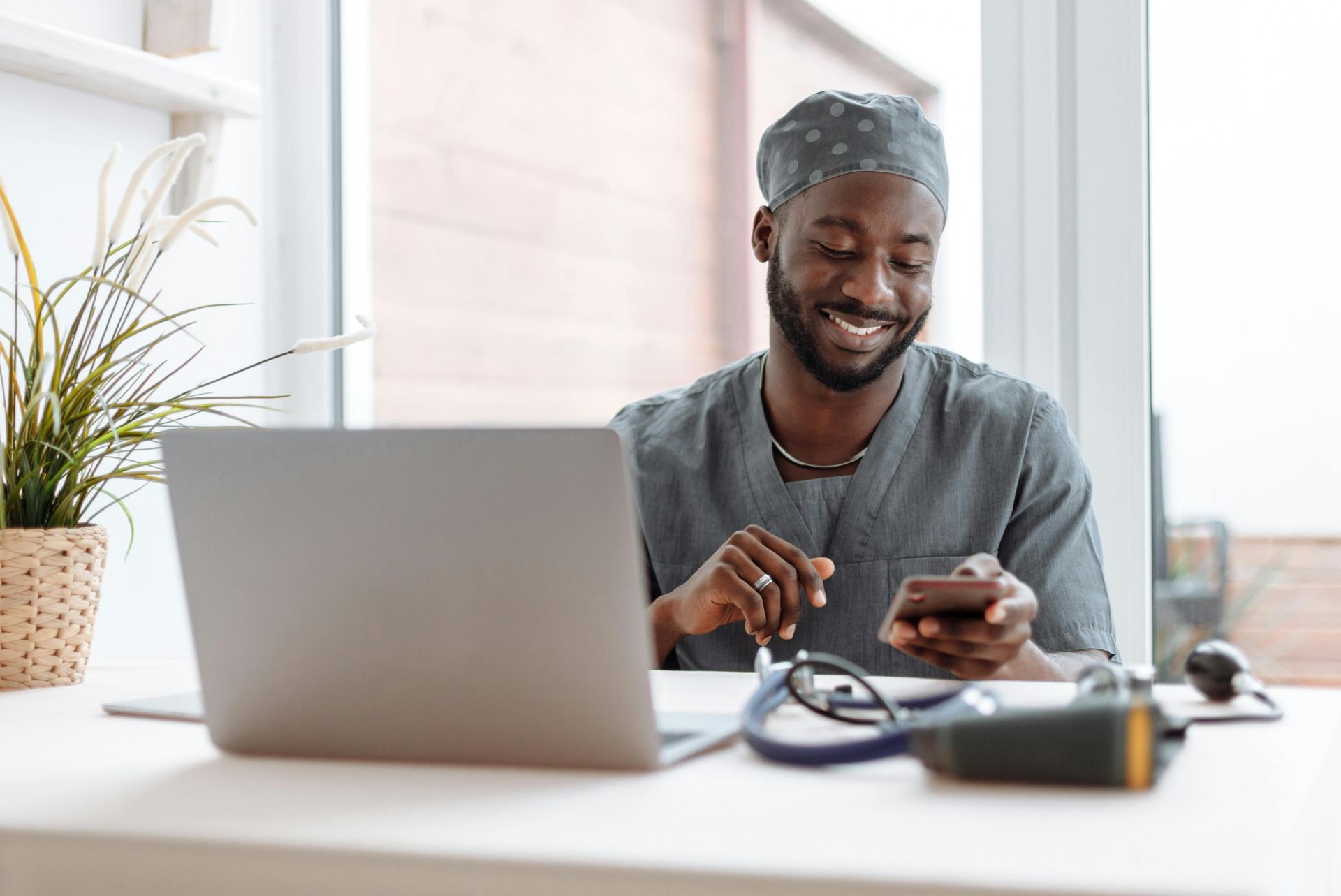 Smiling healthcare professional using phone in office with laptop and medical tools.