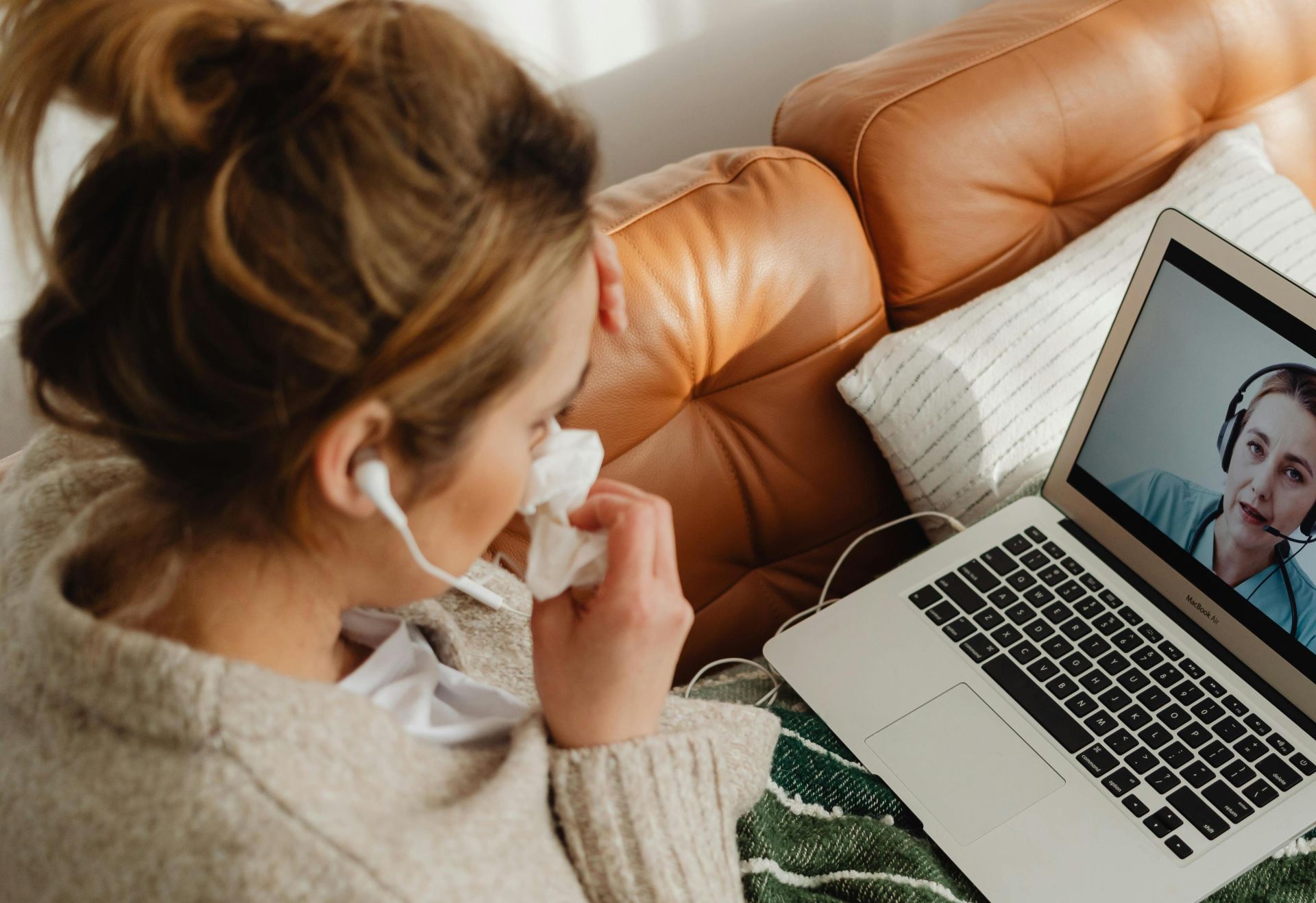 Woman having an online medical consultation on a laptop from her cozy sofa.